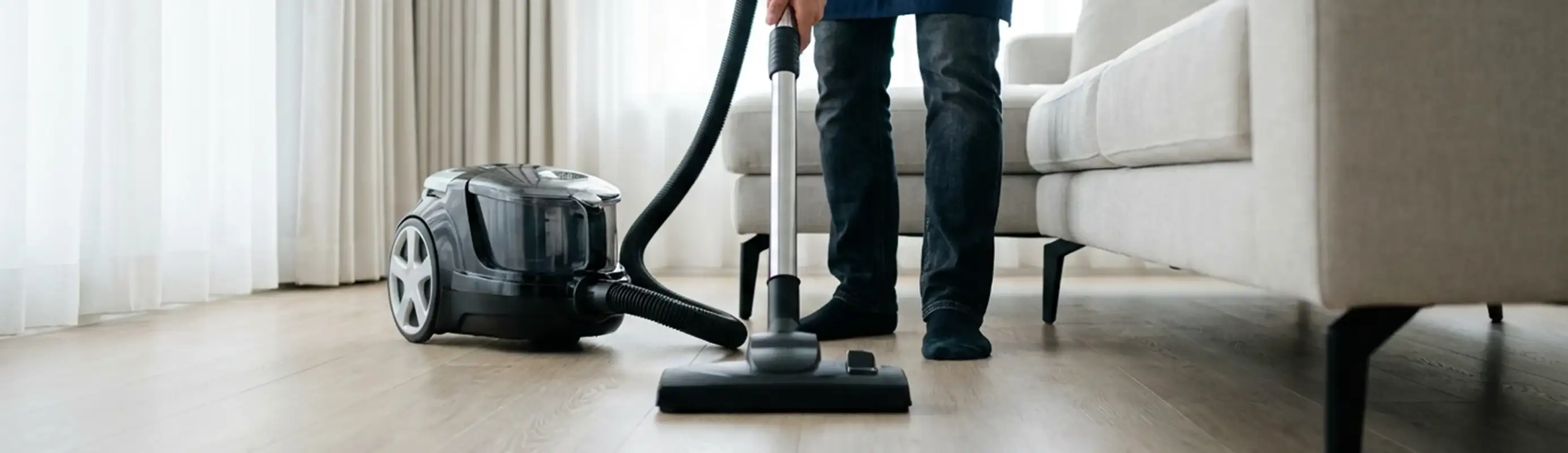 Professional house cleaner vacuuming a living room floor with a canister vacuum cleaner, Aurora, CO.