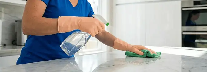 Maid service worker spraying and wiping a kitchen countertop with a microfiber cloth for sanitizing, Aurora, CO.