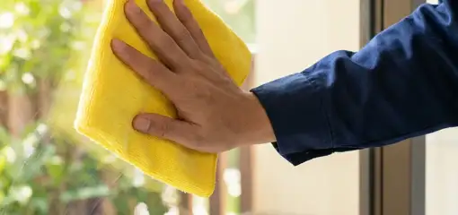 House cleaner wiping a glass window with a yellow microfiber cloth for streak-free cleaning, Aurora, CO.